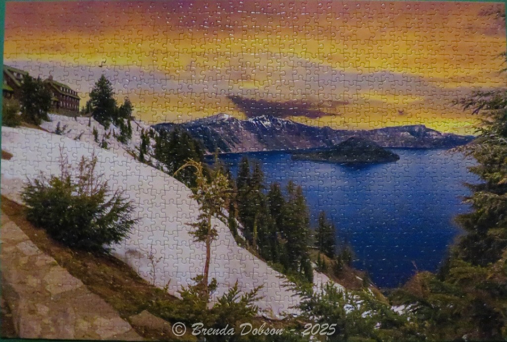Crater Lake National Park at sunrise with snowy slopes, trees, and deep blue water.