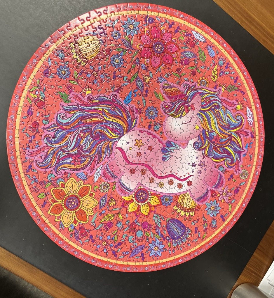 Circular illustration of a whimsical unicorn surrounded by flowers in vibrant pinks and reds.