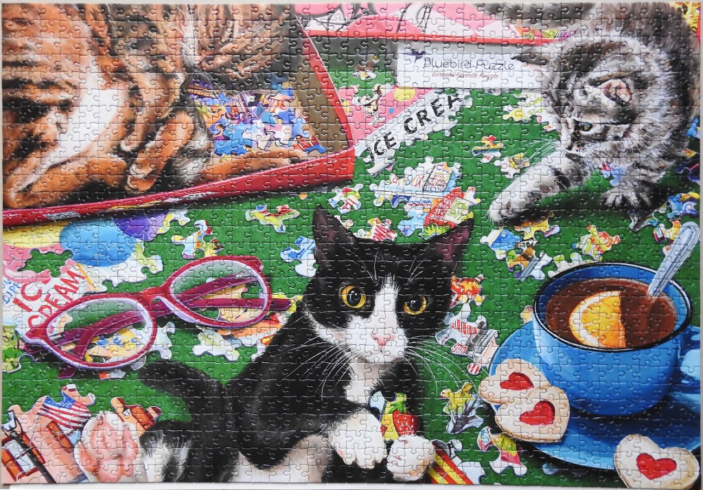 A whimsical illustration of three cats among scattered objects, snacks, and a cup of tea on a green surface.