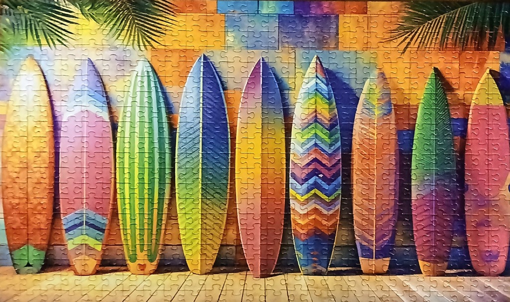 A row of nine vibrant surfboards propped against a colorful tile wall with palm fronds overhead.