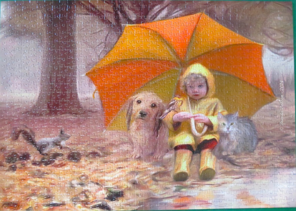 A young child in a yellow raincoat sits under a large orange umbrella with a dog, cat, and squirrel in a park.