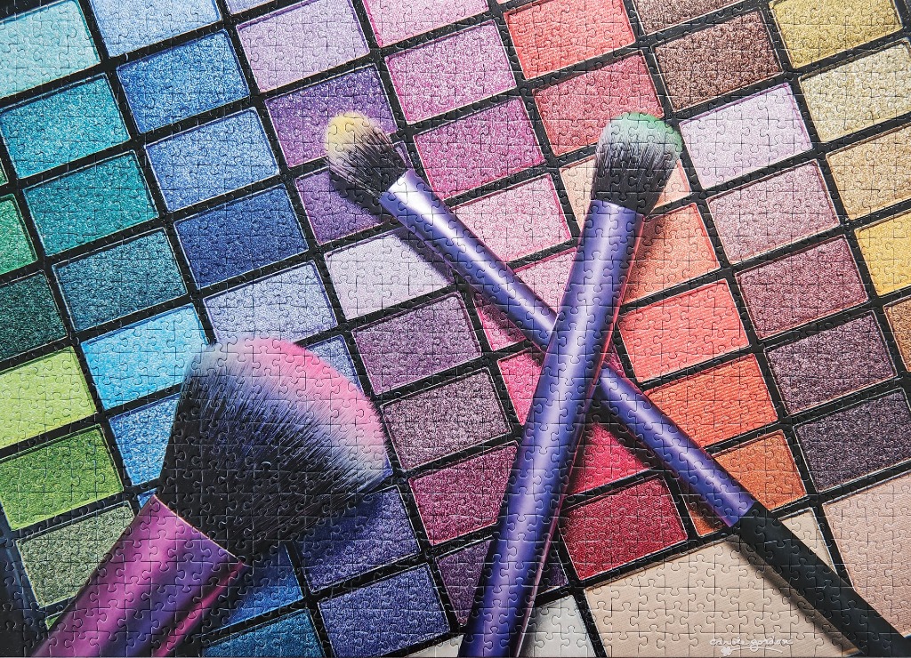 Three makeup brushes resting on a large, multi-colored eyeshadow palette.