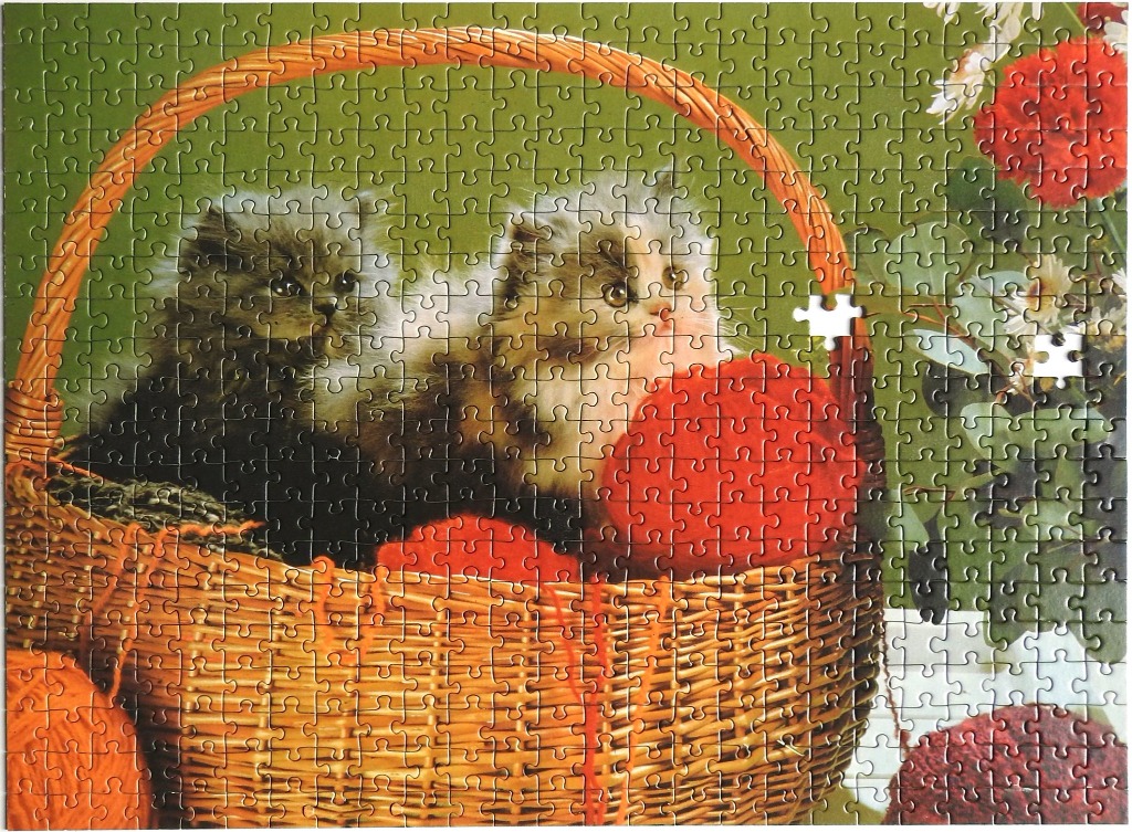 Two fluffy kittens sitting in a wicker basket with balls of yarn and red flowers