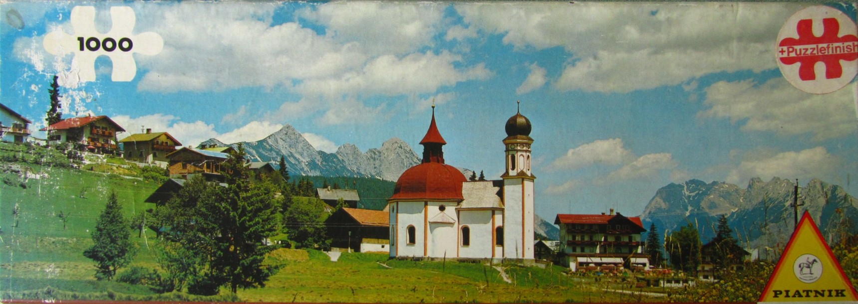 A panoramic alpine scene featuring a white church with a red dome in a green mountain valley under a blue sky.