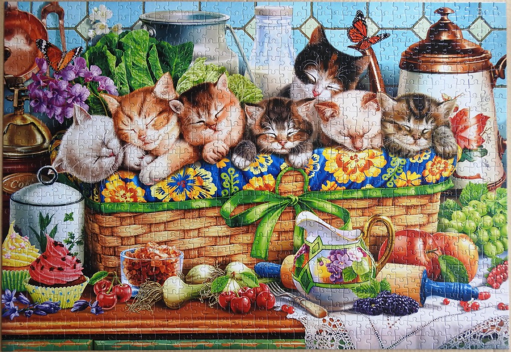 Six kittens sleeping inside a wicker basket on a kitchen counter filled with fresh produce and treats.