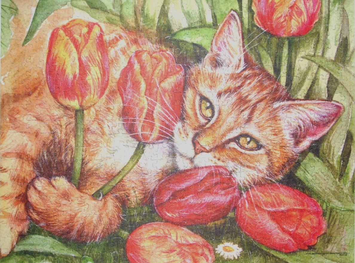 An orange tabby cat resting in a garden among red and yellow tulips.