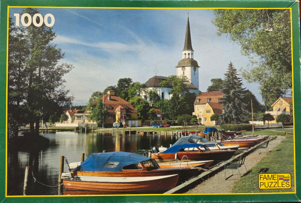 A peaceful Swedish waterfront scene with small motorboats docked in front of a church and yellow houses.