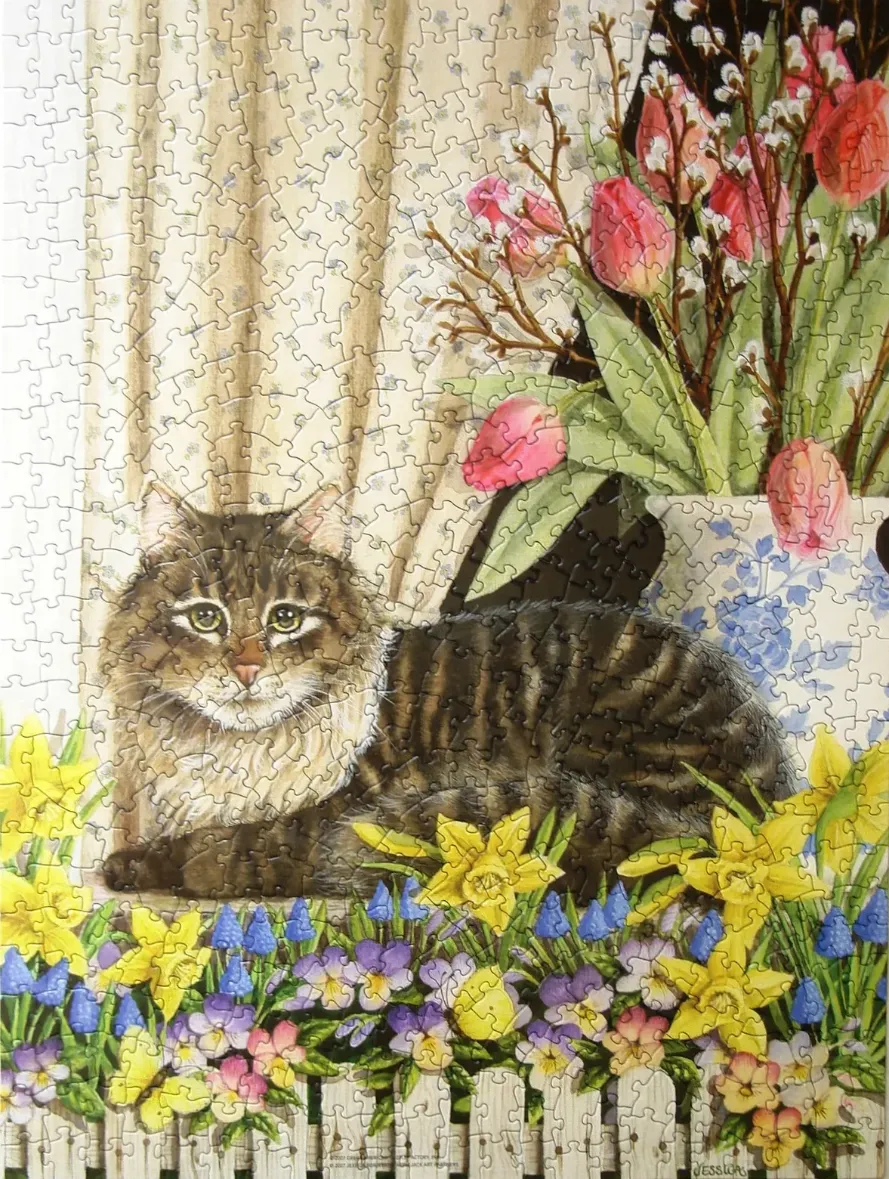 A fluffy tabby cat resting near a window with spring flowers and a white picket fence.