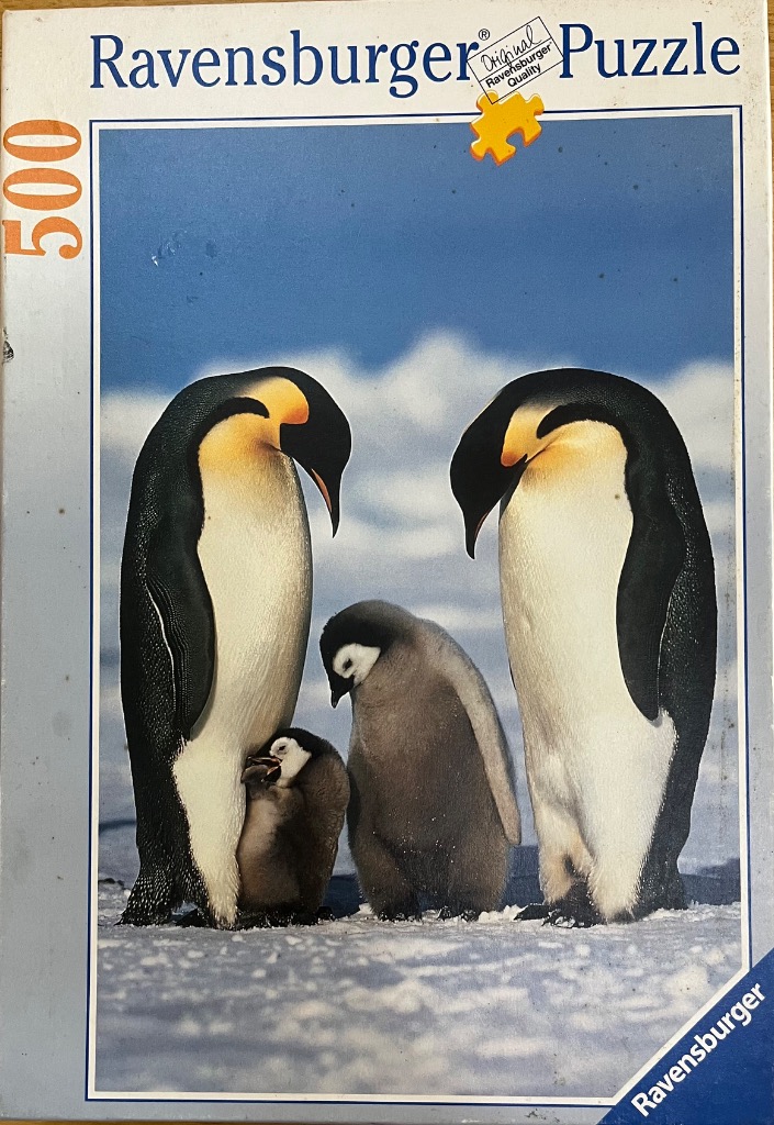 Two adult emperor penguins standing over a chick and a juvenile penguin on a snowy Antarctic landscape.