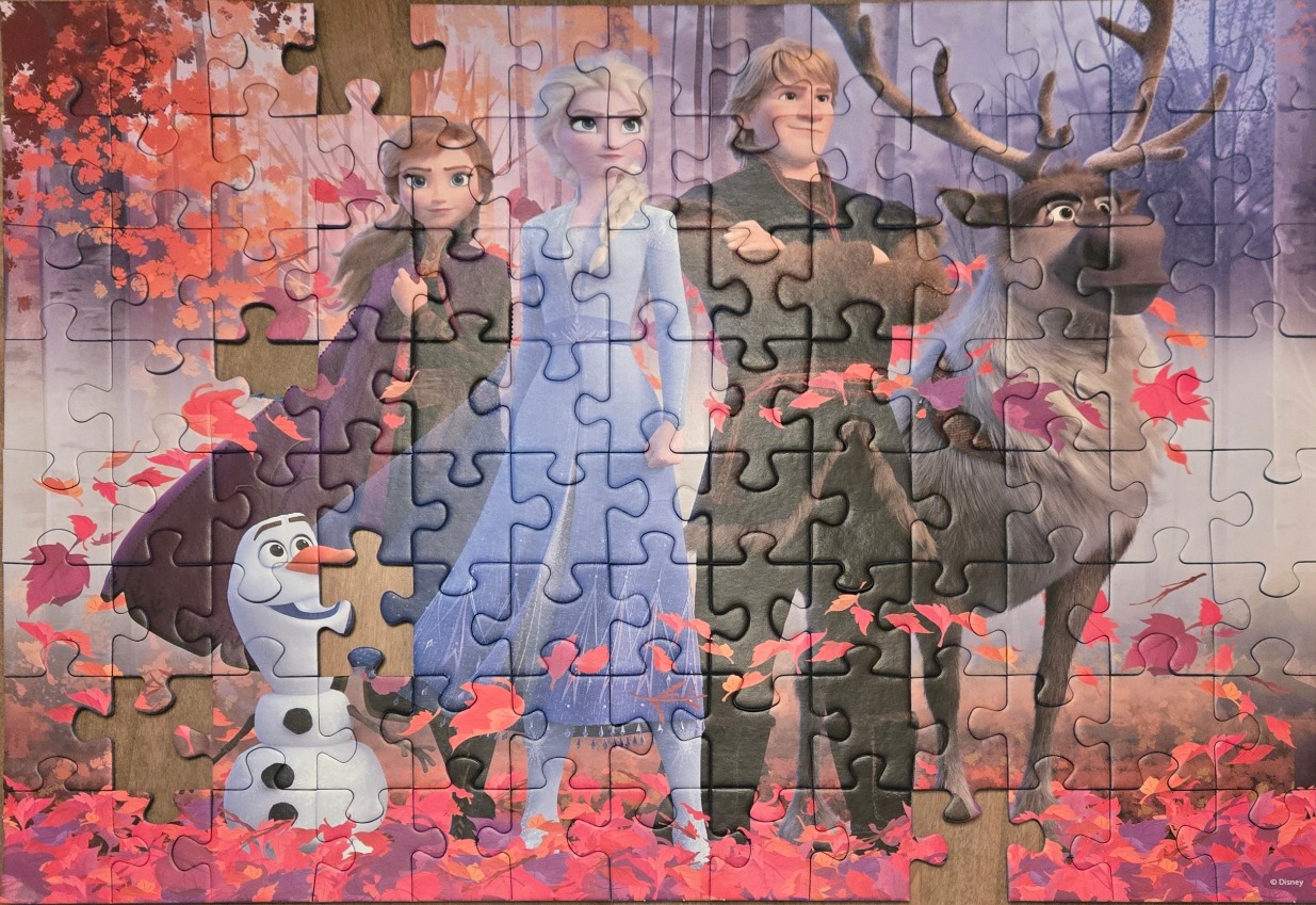 The characters from Frozen 2 stand in an autumn forest filled with falling red and orange leaves.