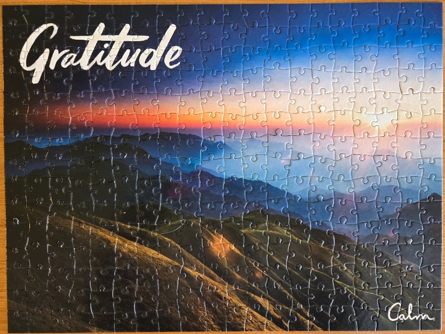 A scenic mountain landscape at sunrise with the word Gratitude written in white script in the top left corner.