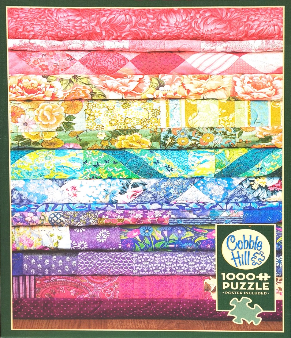 A stack of folded colorful fabric quilts arranged in a rainbow gradient of pink, yellow, blue, and purple patterns.
