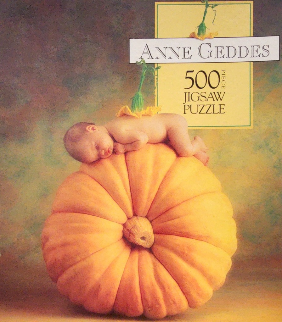 A newborn baby sleeping on top of a large orange pumpkin against a soft, textured background.