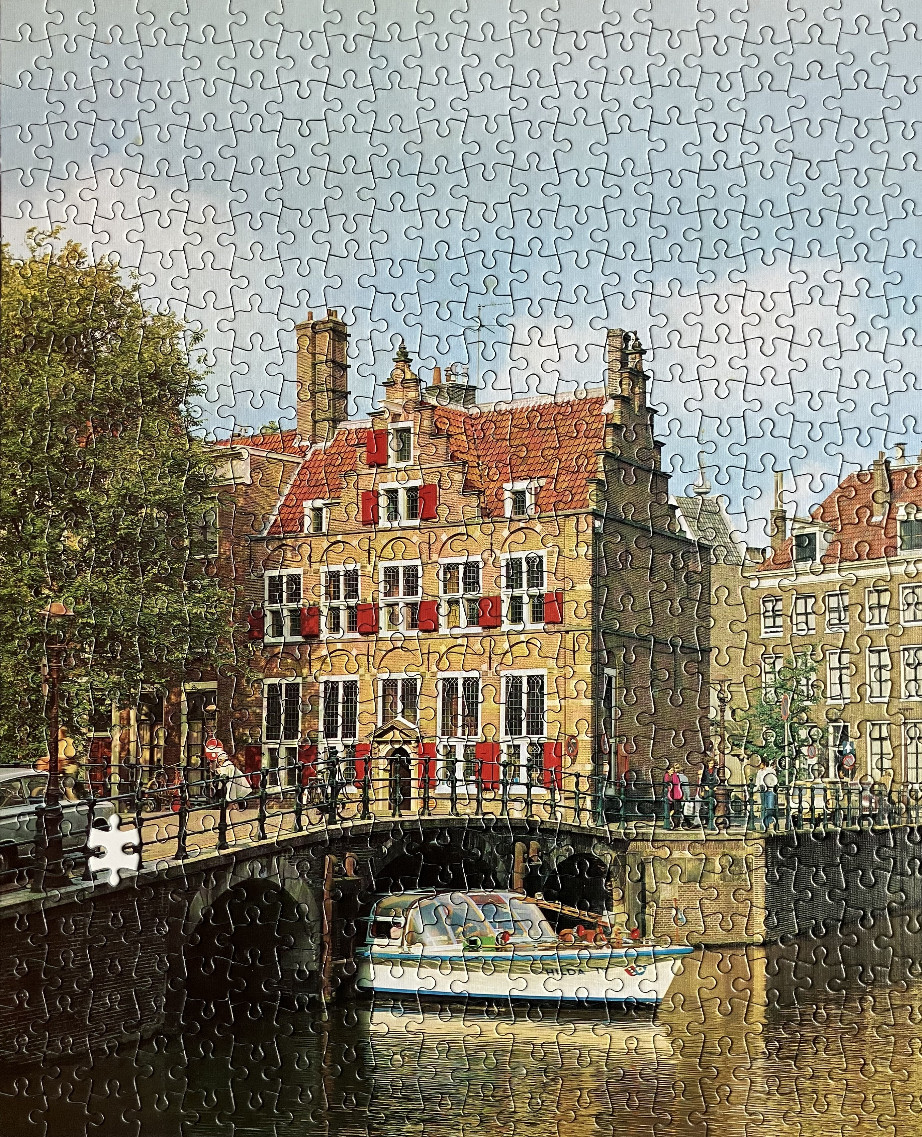 A classic Dutch canal scene with a historic gabled house, a stone bridge, and a tour boat in sunlight.