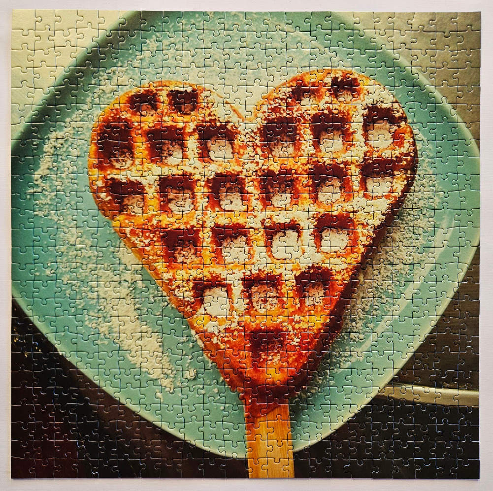 A heart-shaped waffle on a blue plate dusted with powdered sugar.