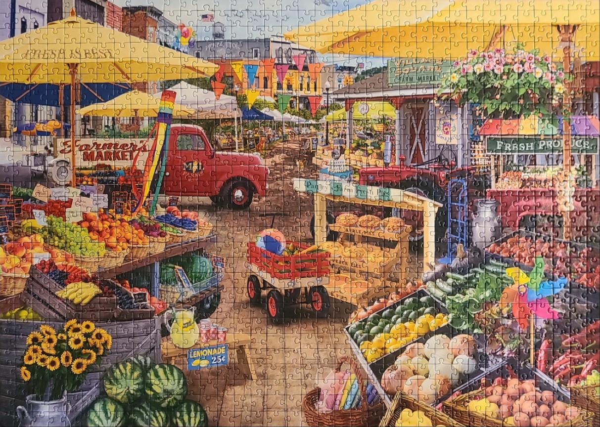 A bustling outdoor farmers market with produce stalls, a red truck, and a red wagon on a village street.