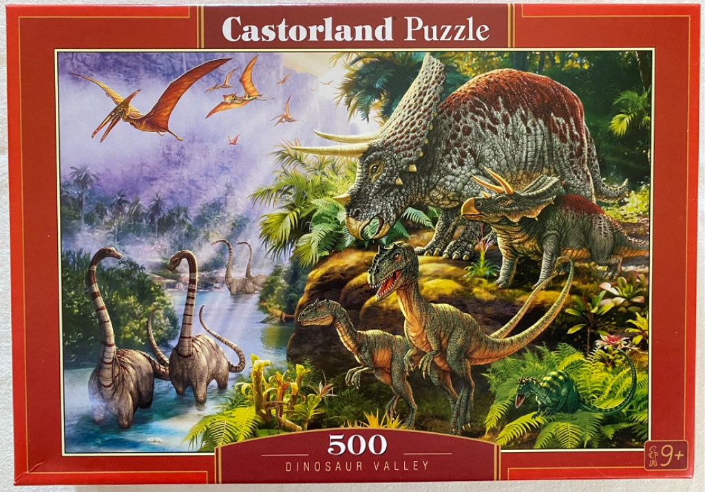 A lush prehistoric valley scene featuring triceratops, raptors, and long-necked dinosaurs near a river.