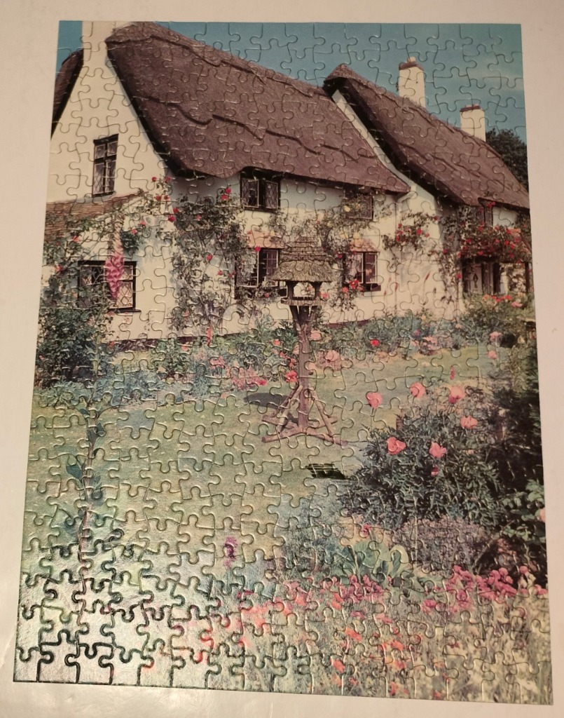 A charming English thatched-roof cottage with a lush flower garden and birdhouse.
