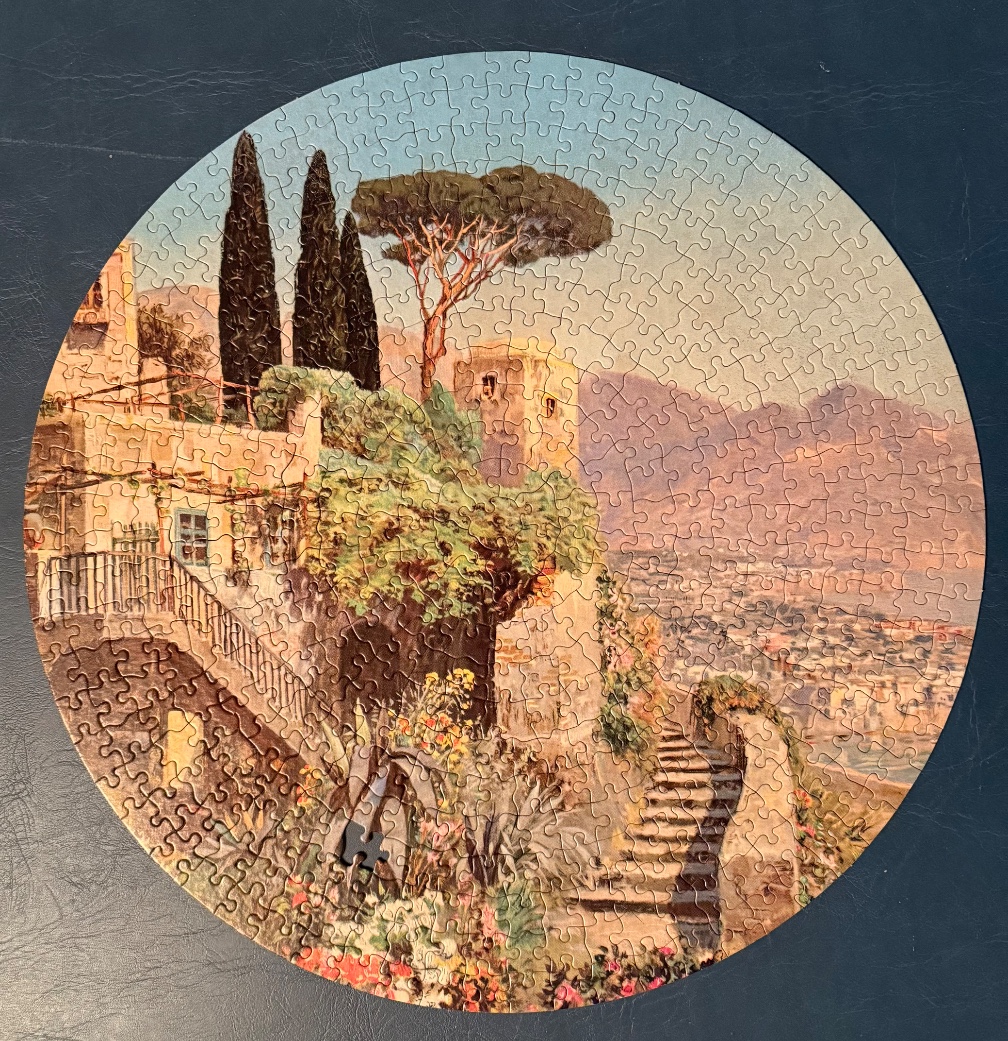 A round painting of a Mediterranean hilltop village with stone stairs, cypress trees, and a mountain backdrop.