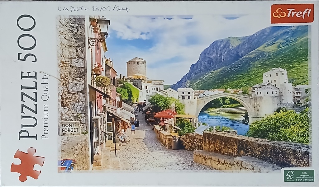 A sunny, historic cobblestone street in Mostar leading to the iconic stone arch bridge over the blue river.