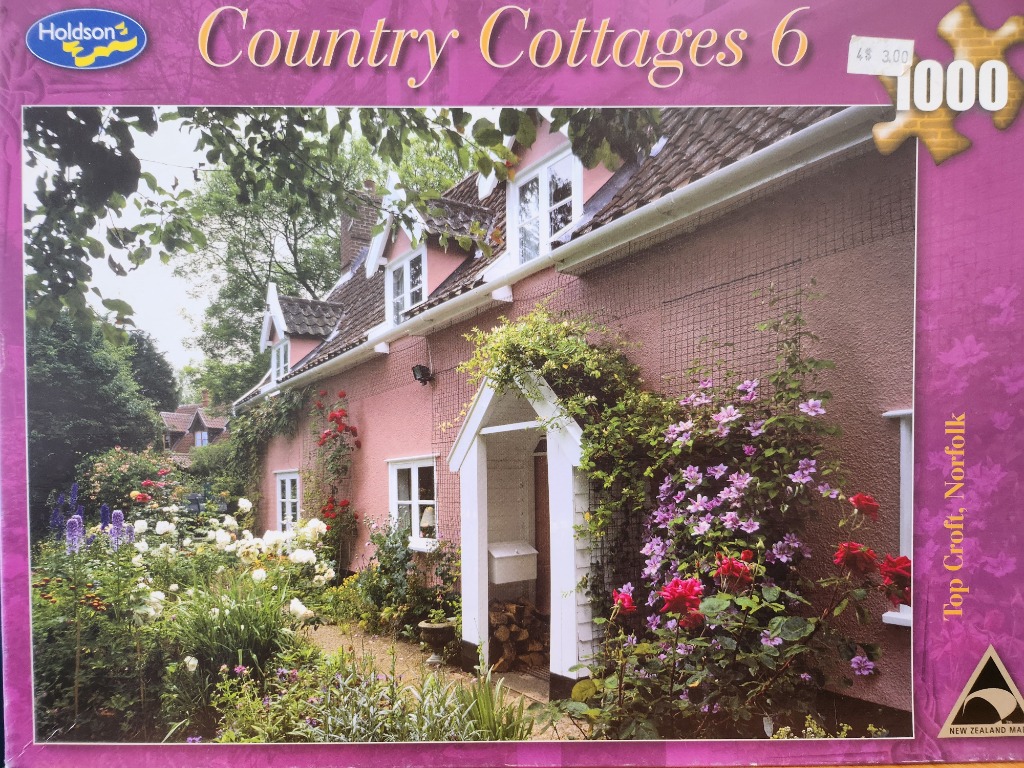 A charming pink cottage with white trim and a lush garden in Norfolk, England.