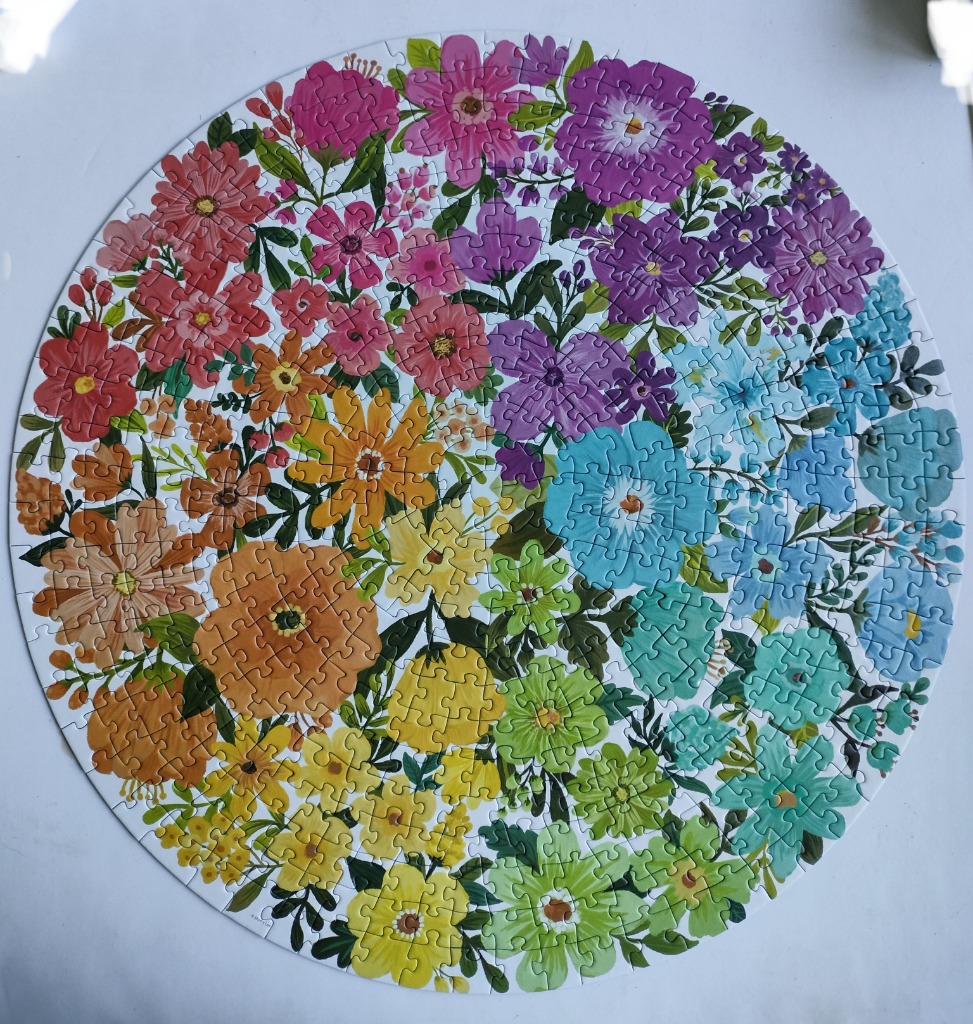 A circular illustration of a vibrant floral arrangement in a rainbow colour gradient.