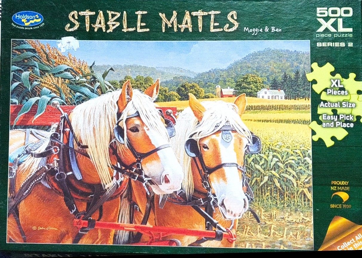 Two chestnut horses with white manes harnessed to a red cart in a farm field.
