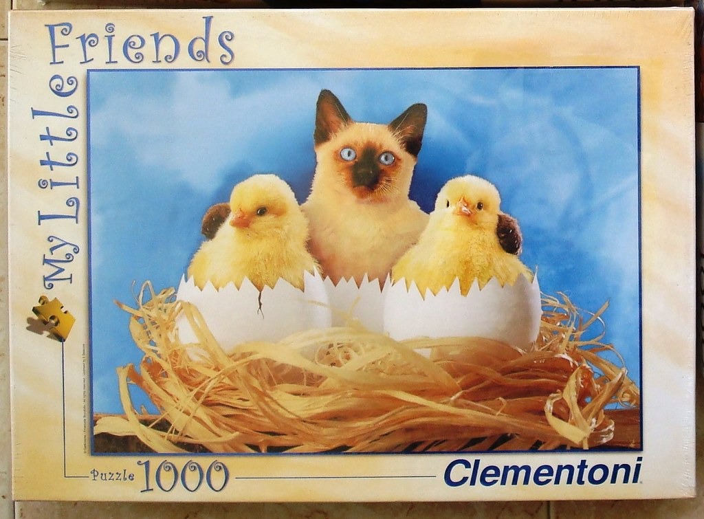 A Siamese kitten sitting in a nest between two baby chicks hatching from eggs against a blue background.