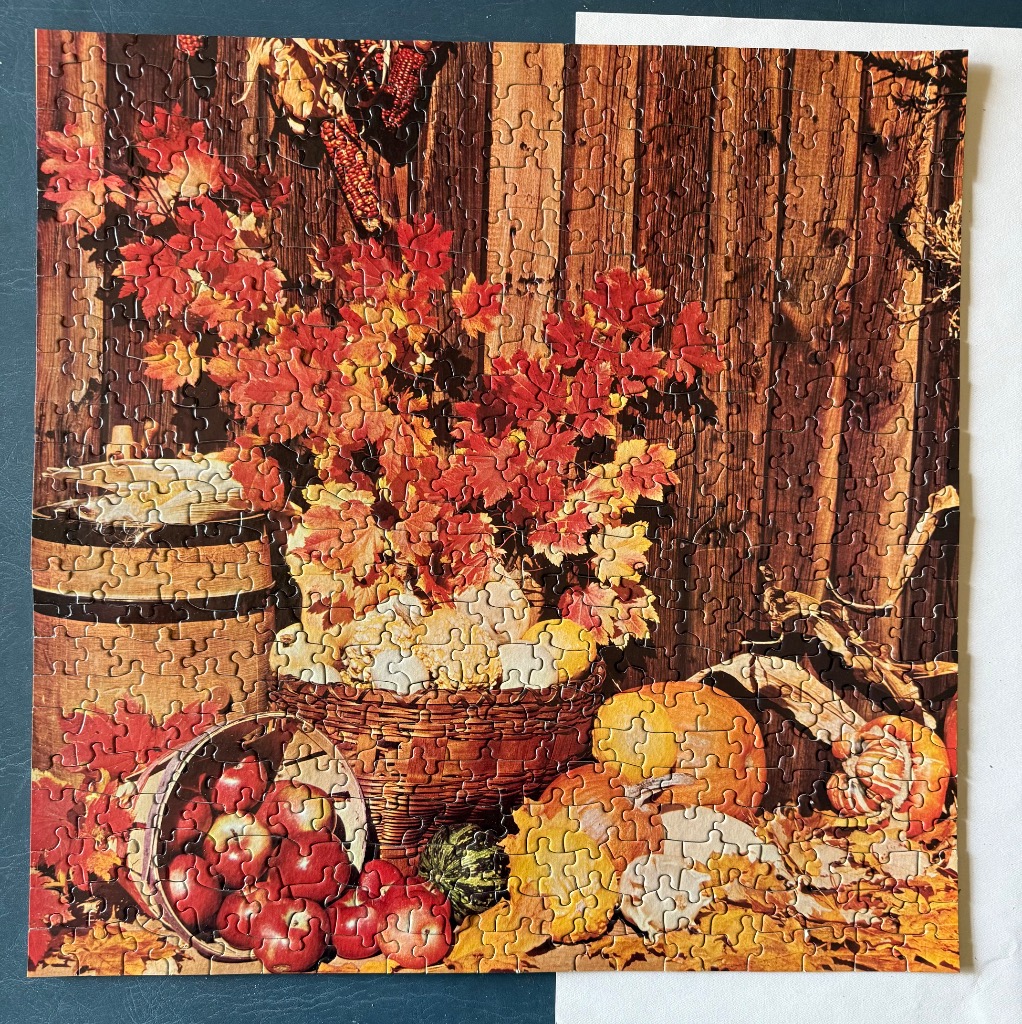 Autumn harvest still life featuring a basket of apples, pumpkins, and vibrant fall leaves against a rustic wooden wall.