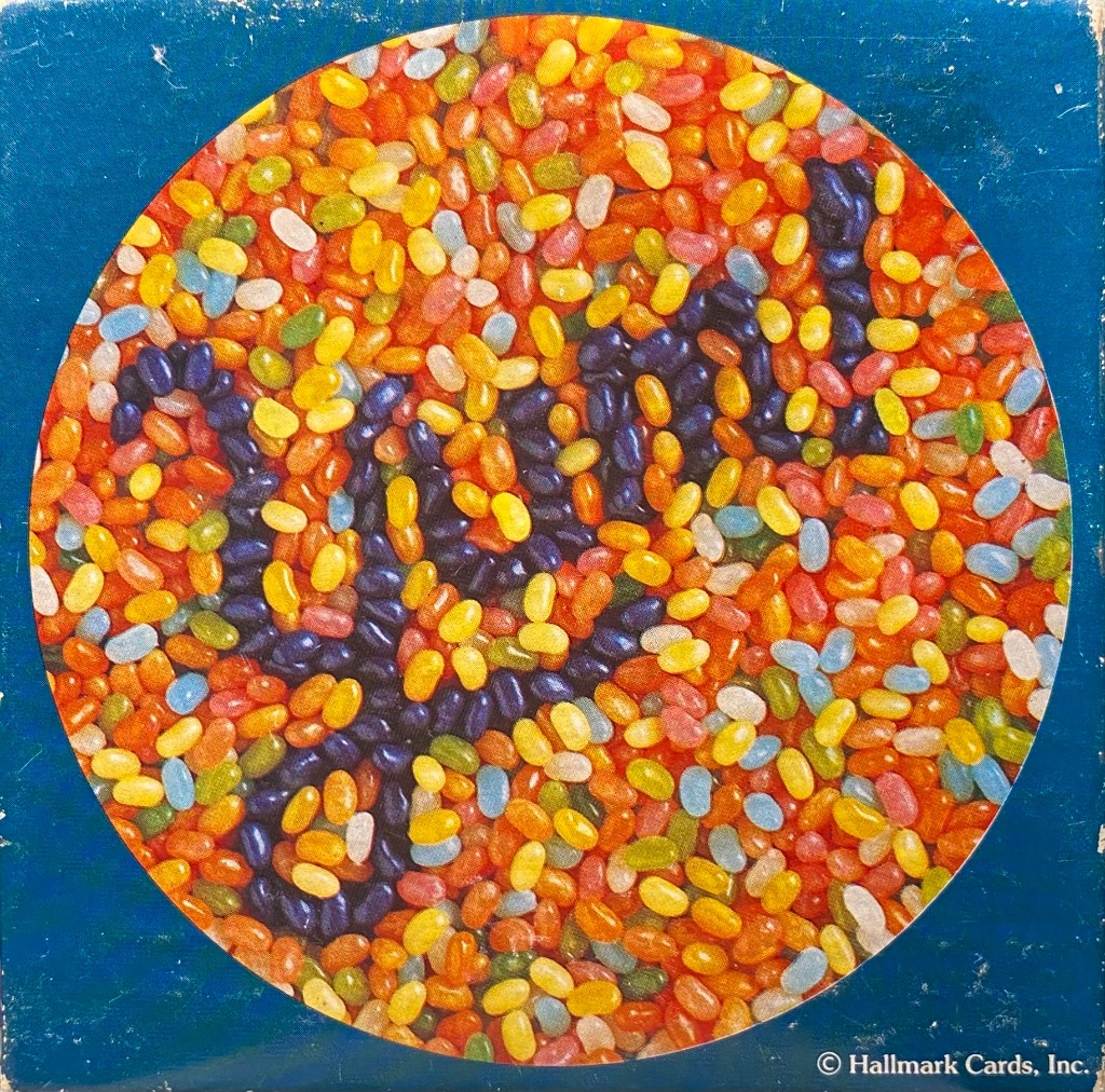 A circular collage of colorful jelly beans arranged to form the cursive word LOVE against a dark blue background.