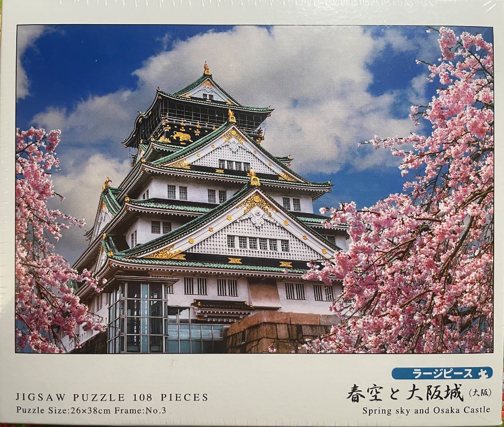 Osaka Castle rising behind vibrant pink cherry blossom branches under a blue, cloudy sky.