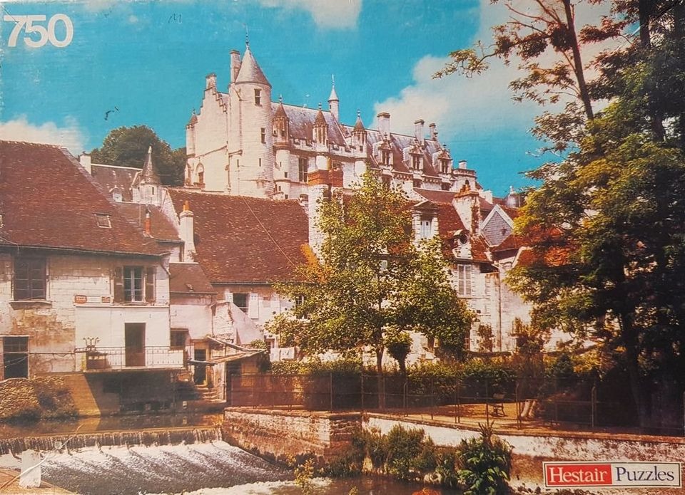 A French-style chateau rising above historic stone houses and a small waterfall.