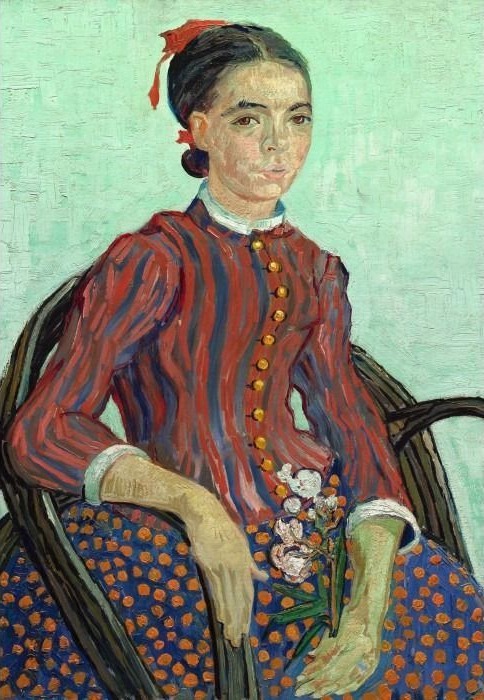 A woman with dark hair and a red ribbon sits in a chair wearing a striped blouse and a polka-dot skirt.