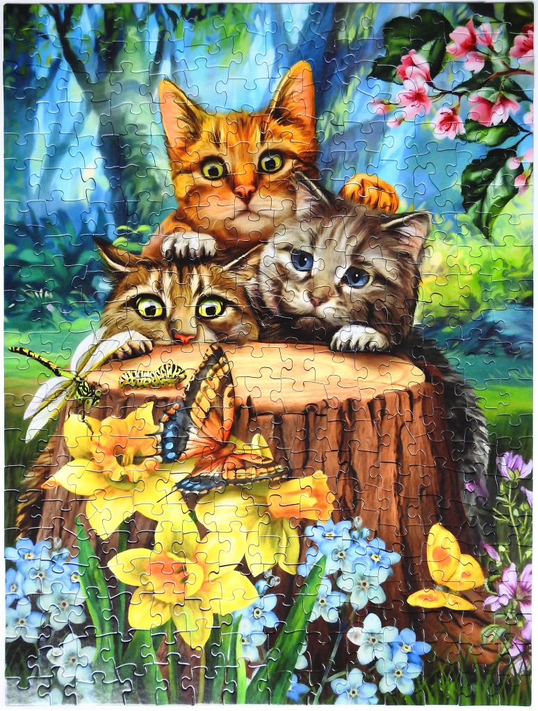 Three kittens peeking over a tree stump in a garden with butterflies and flowers.