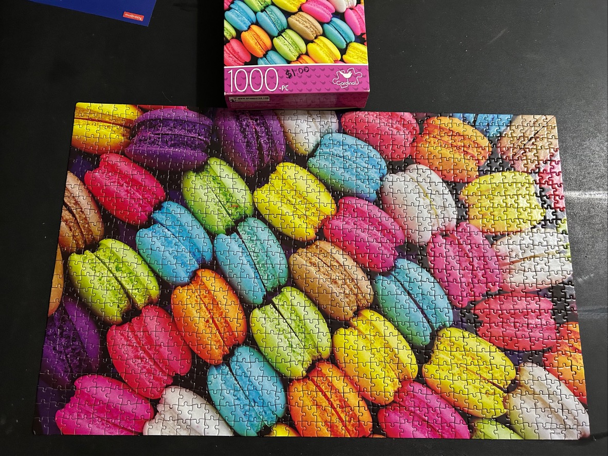 A vibrant, overhead display of dozens of colorful French macarons arranged in a repeating pattern.