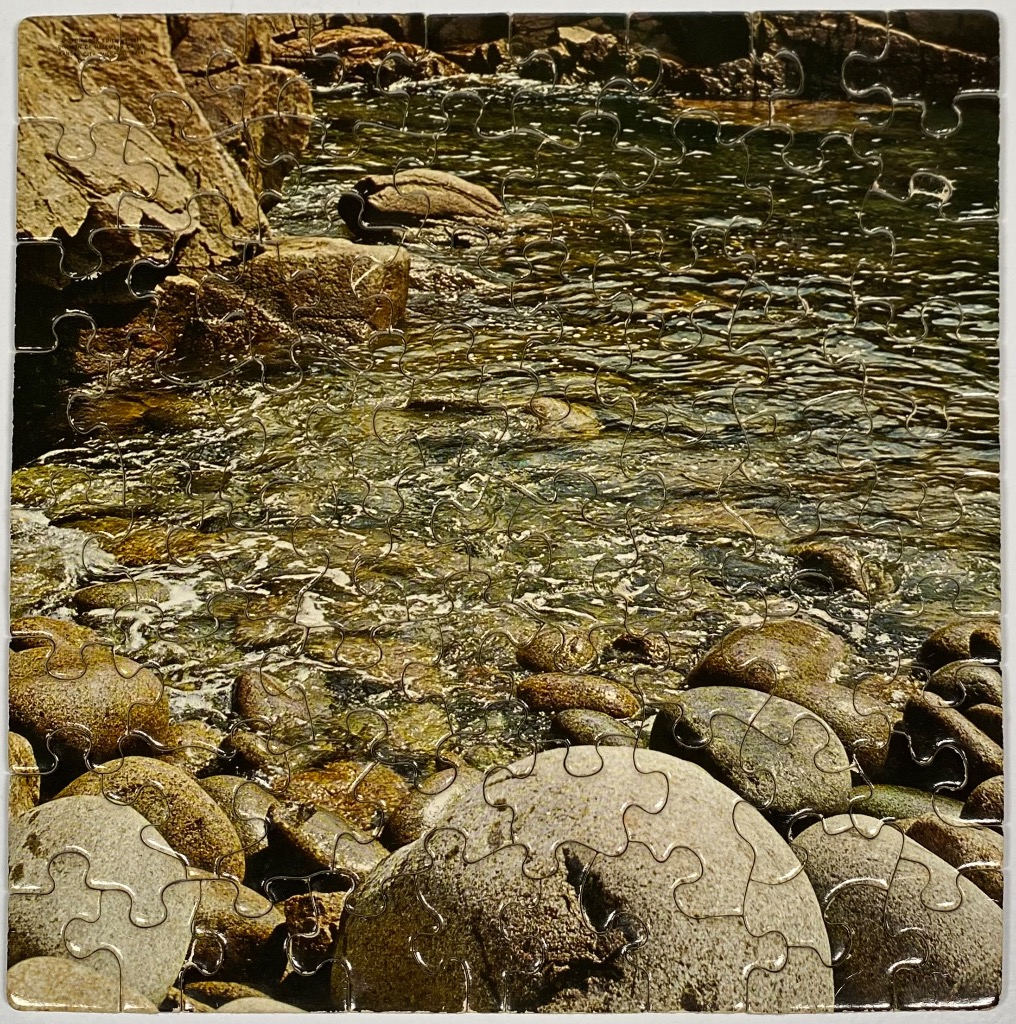 A rocky shoreline meeting shallow, clear water with light reflecting off the ripples.