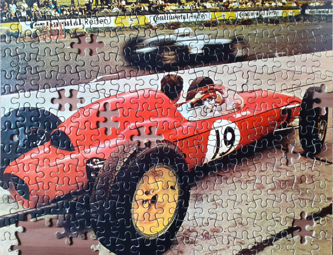 A vintage red race car number 19 on a track with spectators in the background.