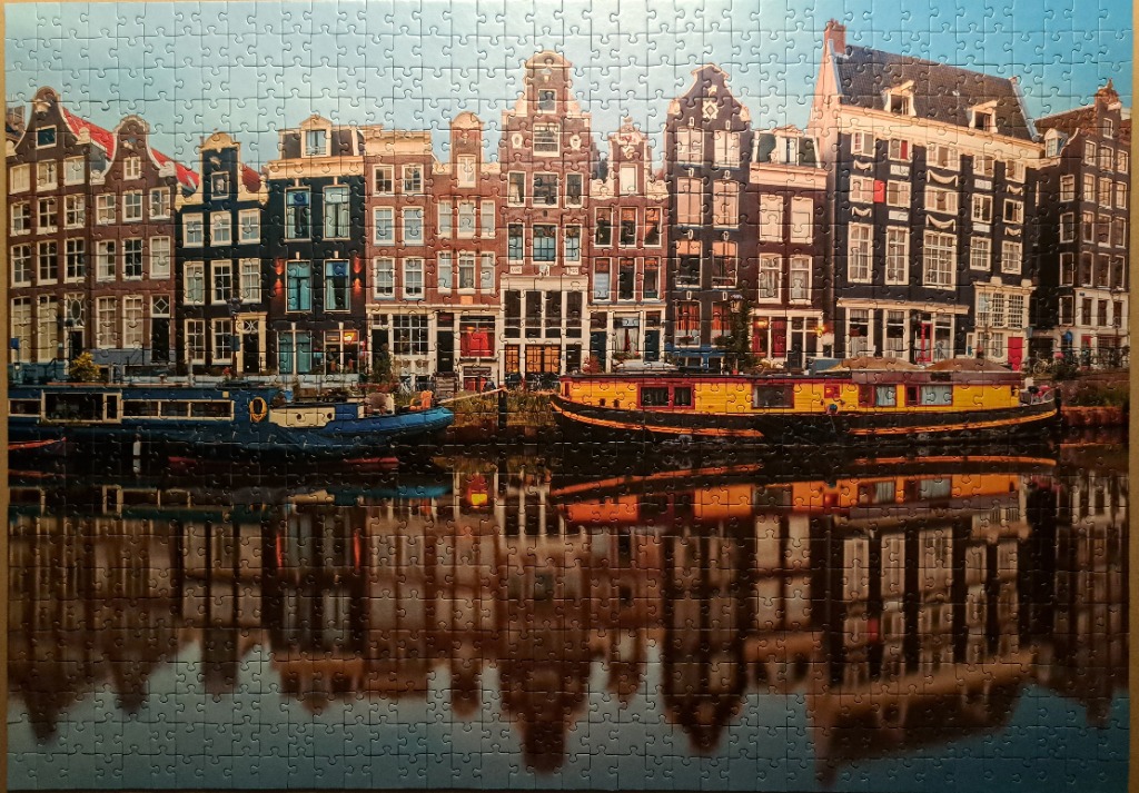 A row of historic canal houses in Amsterdam reflected in the water with two houseboats in the foreground.