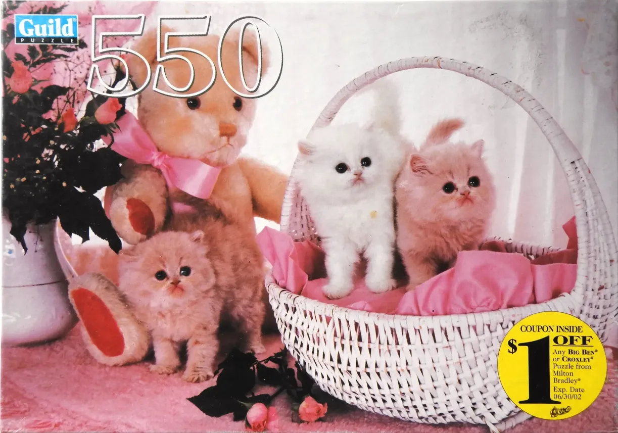 Three fluffy kittens with a teddy bear in a white wicker basket decorated with pink accents.
