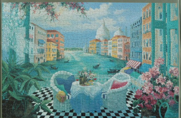 A balcony with two chairs and a table overlooking a Venetian canal with historic buildings and gondolas.