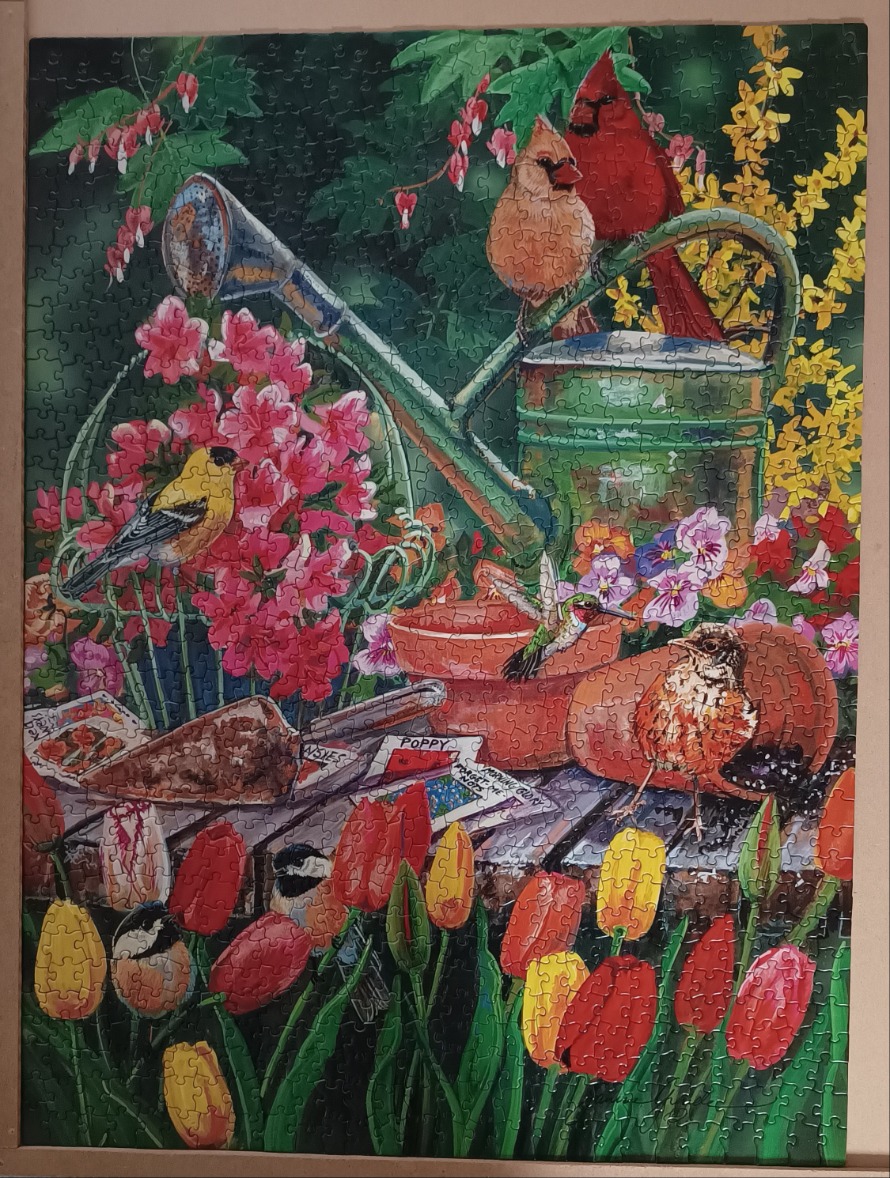 A garden scene featuring songbirds, a metal watering can, and various spring flowers.
