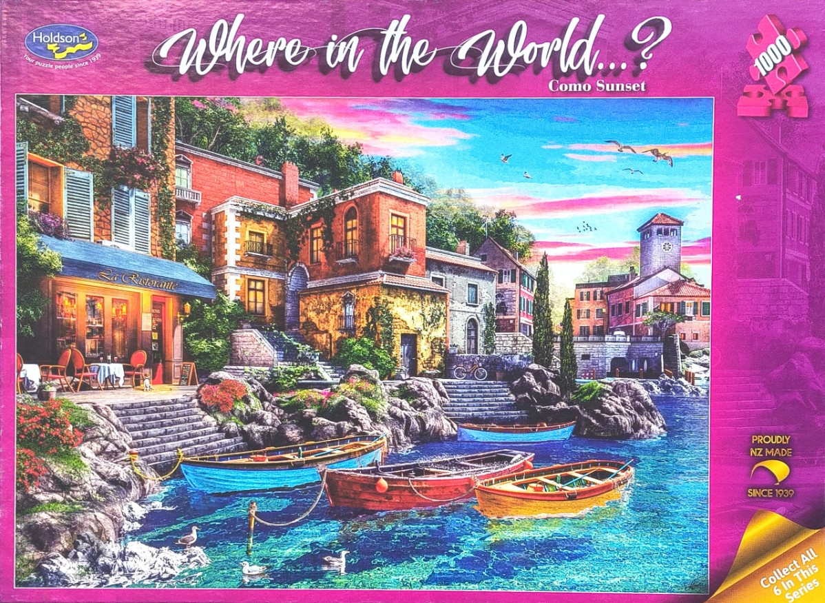 A scenic lakeside village at sunset with colorful boats moored at stone stairs below restaurant terraces.