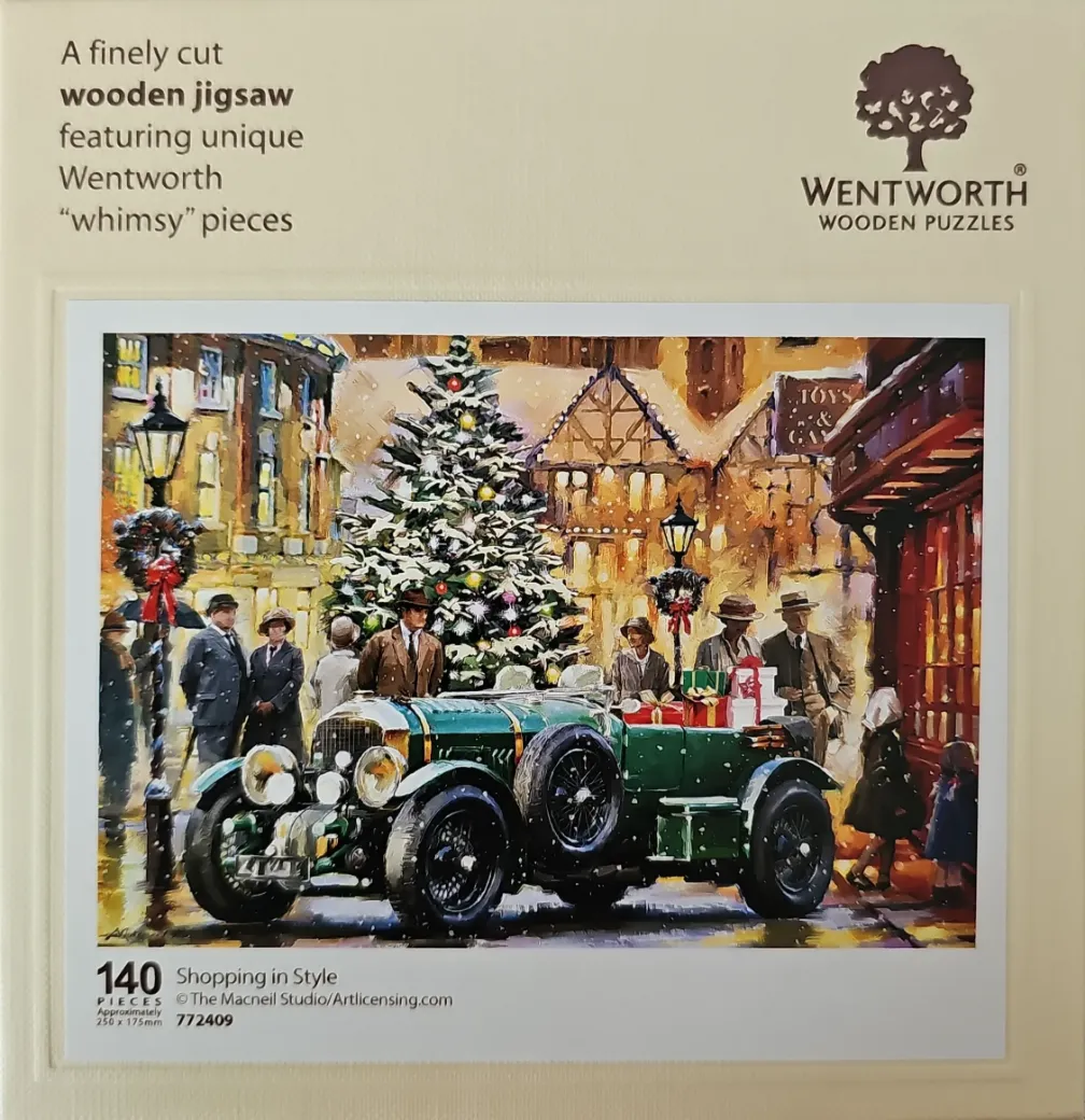 A vintage green car parked in a snow-covered town square during Christmas, surrounded by people and a large tree.