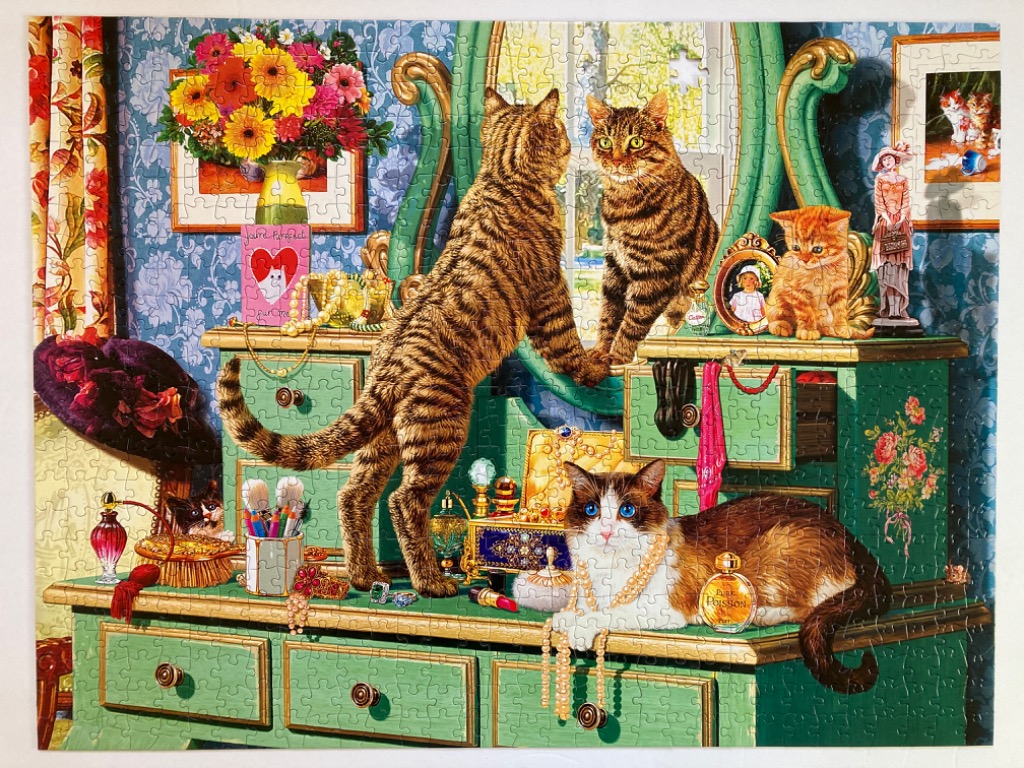 Three cats interacting on and around a vintage green vanity filled with jewelry and makeup.