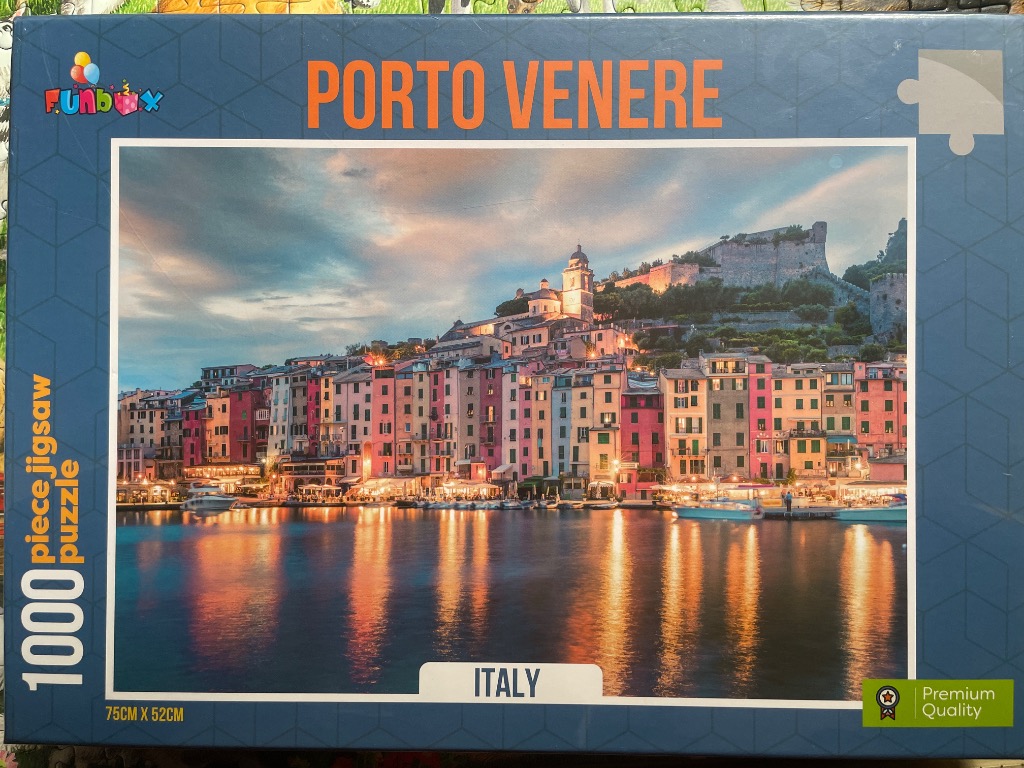 A panoramic photograph of the colorful hillside village of Porto Venere, Italy, reflected in the calm harbor at twilight.