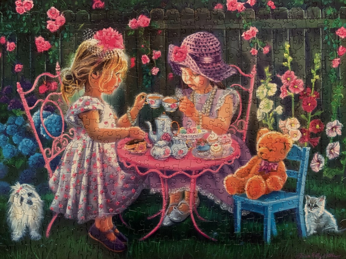 Two young girls in fancy dresses and hats having a tea party in a rose garden with a teddy bear, a kitten, and a puppy.