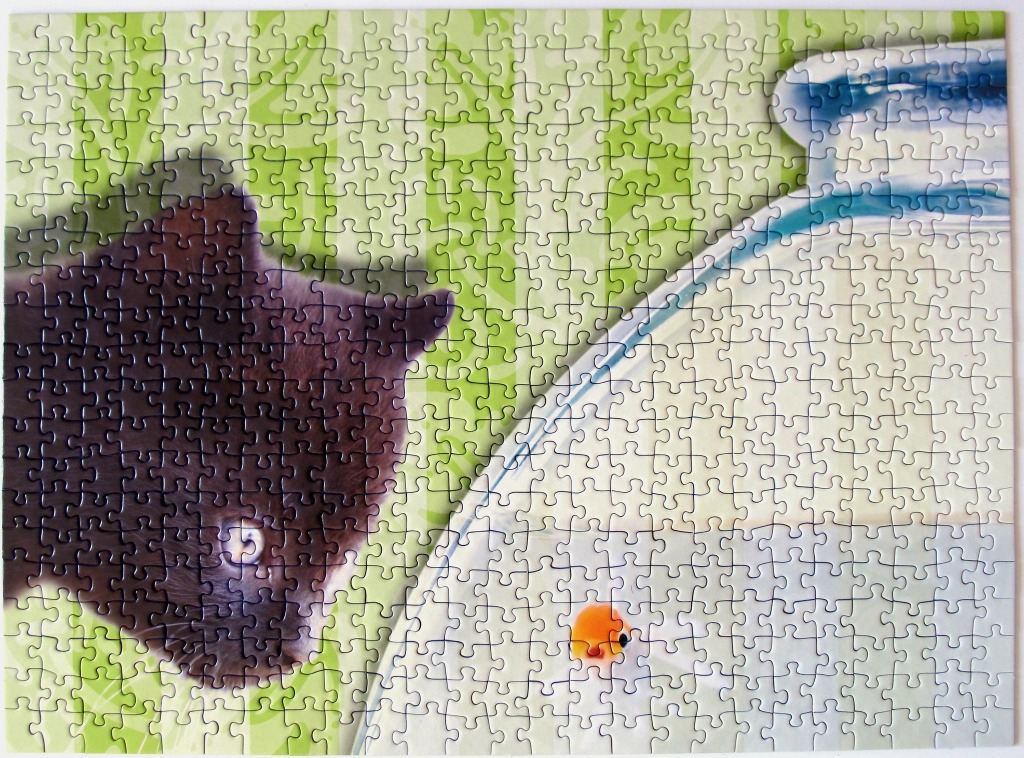 A close-up view of a curious black kitten looking into a fishbowl with a small orange goldfish inside.