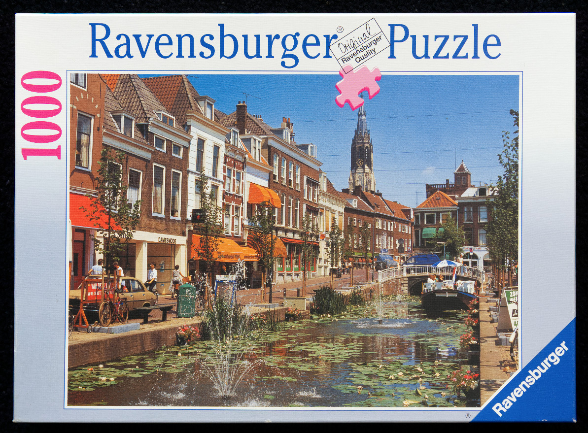 A sunny Dutch canal scene with historic brown brick buildings, lily pads, and a tall church spire in the background.