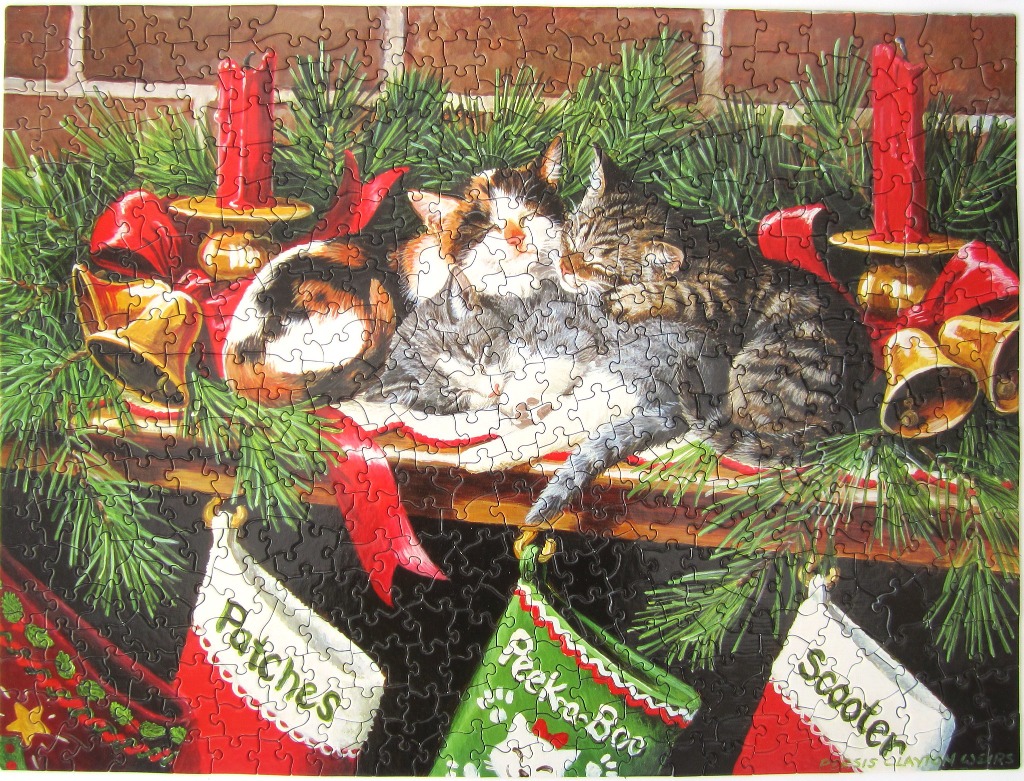 Two kittens sleeping on a Christmas mantelpiece with stockings and candles