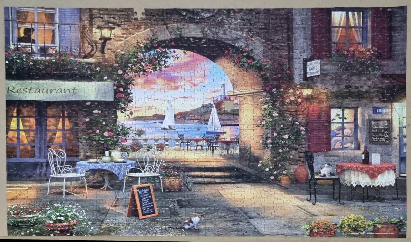 A Mediterranean seaside restaurant patio viewed through a stone archway at sunset.